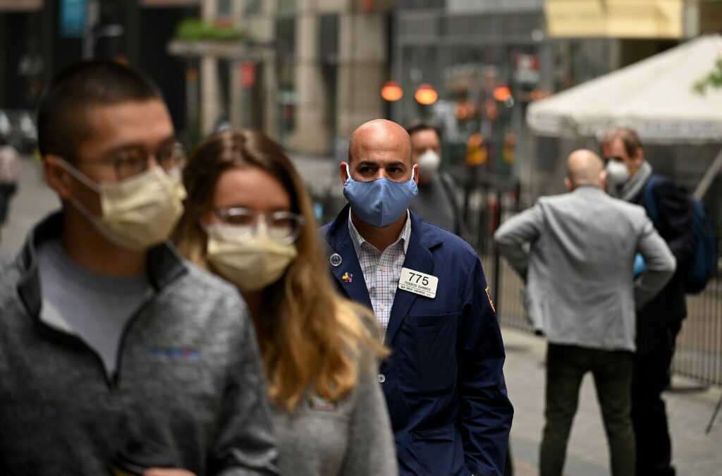 A trader walks in front of the New York Stock Exchange (NYSE) on May 26, 2020 at Wall Street in New York City. - Wall Street stocks surged early May 26, 2020 on optimism about coronavirus vaccines as the New York Stock Exchange resumed physical floor trading for the first time since late March. About five minutes into trading, the Dow Jones Industrial Average was up 2.3 percent at 25,023.76. The broad-based S&P 500 gained 2.0 percent to 3,013.04, while the tech-rich Nasdaq Composite Index advanced 1.6 percent to 9,468.96.The gains came after a ceremony presided over by New York Governor Andrew Cuomo, who wore a mask as he rung the opening bell to signal the start of the day for traders, also clad in masks and separated by plexiglas. (Photo by Johannes EISELE / AFP) (Photo by JOHANNES EISELE/AFP via Getty Images)